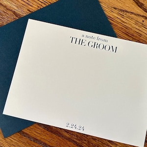 May include: A white card with a navy blue envelope. The card says "a note from THE GROOM" and "2.24.24".