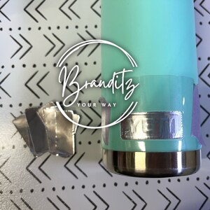 May include: A teal tumbler with a silver base and a silver label is shown. The tumbler has a silver label with the text "Branditz YOUR WAY" in a white script font. Several silver labels are to the left of the tumbler.