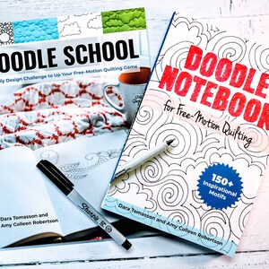 May include: Two books titled "Doodle School: A Daily Design Challenge to Up Your Free-Motion Quilting Game" and "Doodle Notebook for Free-Motion Quilting" by Dara Tomasson and Amy Colleen Robertson. The books are open and show black and white doodle designs.