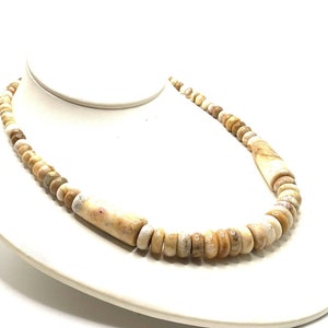May include: A beige and brown stone bead necklace with a larger, cylindrical bead in the center.