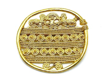 May include: A circular gold brooch with intricate Celtic knotwork and a central design of two stylized figures. The brooch is made of a single piece of metal and has a smooth, polished finish.