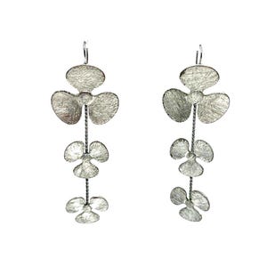 May include: A pair of silver-toned drop earrings. Each earring features three textured, stylized flower shapes connected by a delicate chain. The earrings have a hook closure and hang vertically, creating a dangling effect.