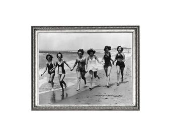 May include: Black and white framed photograph of six women running on a beach. They are wearing vintage swimsuits and holding hands. The ocean and sky are visible in the background. The frame is silver.