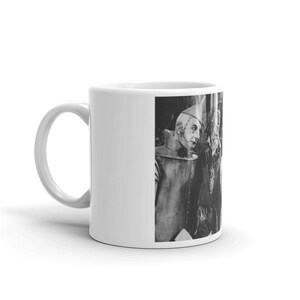 Puede incluir: Una taza de cer&aacute;mica blanca con una imagen en blanco y negro del Hombre de Hojalata del Mago de Oz. El Hombre de Hojalata lleva un traje plateado y un sombrero puntiagudo. Est&aacute; mirando hacia la derecha de la imagen.