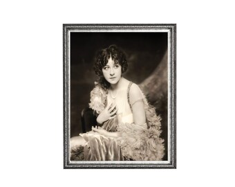 May include: A framed black and white vintage photograph featuring a person with dark curly hair wearing a sleeveless dress and a feathered wrap. The person is adorned with a pearl necklace and is captured in a seated pose within a decorative frame.