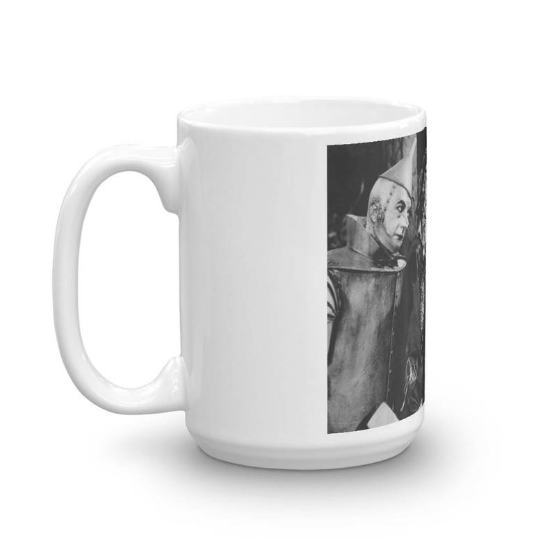 Puede incluir: Una taza de cer&aacute;mica blanca con una imagen en blanco y negro del Hombre de Hojalata de El Mago de Oz. El Hombre de Hojalata lleva un sombrero plateado y un traje plateado. Est&aacute; mirando hacia la derecha.