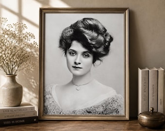 May include: A black and white portrait print of a person with an elaborate updo hairstyle, wearing a lace-trimmed garment and a delicate necklace with a heart-shaped pendant, encased in a thin, metallic gold-toned rectangular frame.