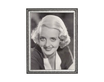 May include: A framed black and white portrait of a woman with light-colored hair styled in soft waves. The woman is smiling, and the frame is silver with a detailed border. The portrait is a vintage piece.