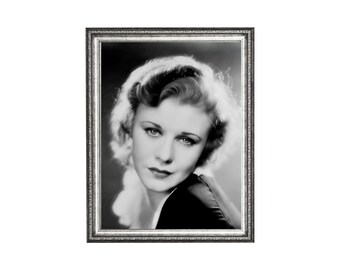May include: Black and white framed portrait of a woman with wavy hair, gazing towards the viewer. The photograph is in a silver-colored frame, adding a vintage aesthetic. The woman is wearing a dark-colored garment.