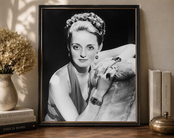 May include: A black and white framed portrait of a person with curled hair, wearing a sleeveless top, earrings, a large ring, and a wide bracelet. The person is leaning on a textured surface, holding a thin object between their fingers.