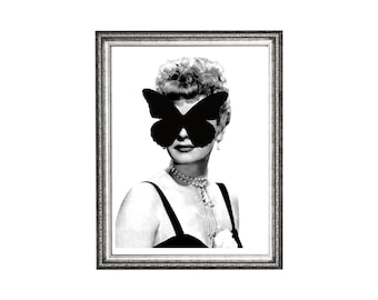 May include: Black and white framed print featuring a woman with a black butterfly covering her eyes. She wears a pearl necklace and a black dress. The frame is silver with a decorative border. The image is a portrait.