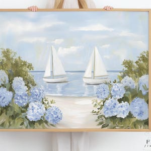 May include: A framed painting featuring two sailboats on a serene beach scene. The artwork showcases blue hydrangeas, lush greenery, and a light blue sky. The painting is in a wooden frame and is held by a person.