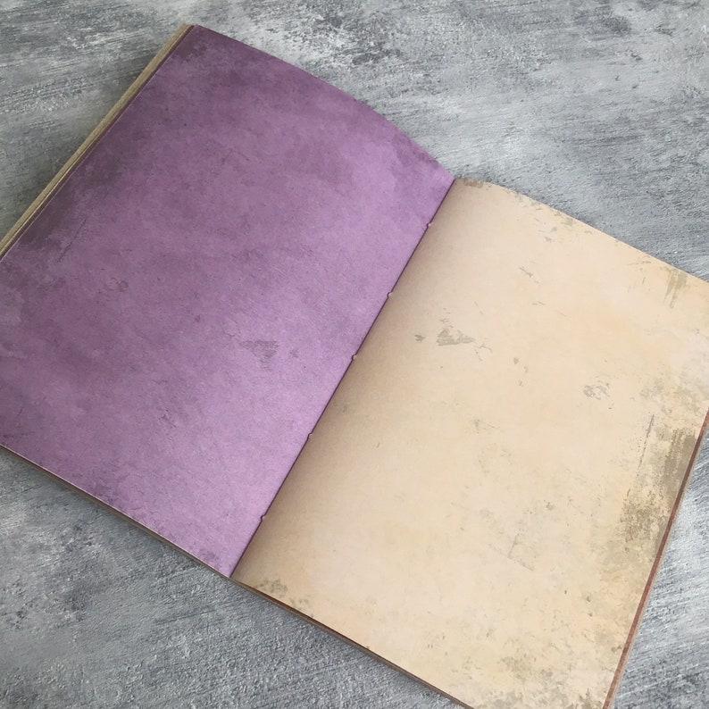 Puede incluir: Un cuaderno abierto con una cubierta morada y una p&aacute;gina en blanco de color crema. El cuaderno tiene un aspecto desgastado y vintage.