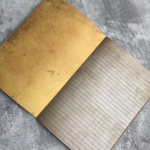 Puede incluir: Un cuaderno con una cubierta dorada y p&aacute;ginas rayadas. La cubierta tiene un aspecto desgastado, lo que le da un toque vintage.