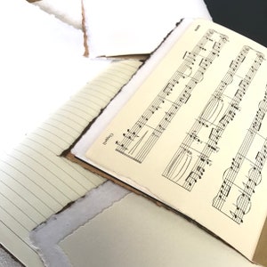 May include: A close-up of a sheet of music with the word "Campbells" printed on it. The music is written in black ink on a white background. The sheet of music is lying on top of a notebook with lined pages.