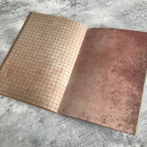 Puede incluir: Un cuaderno abierto con una p&aacute;gina cuadriculada marr&oacute;n a la izquierda y una p&aacute;gina texturizada marr&oacute;n a la derecha.