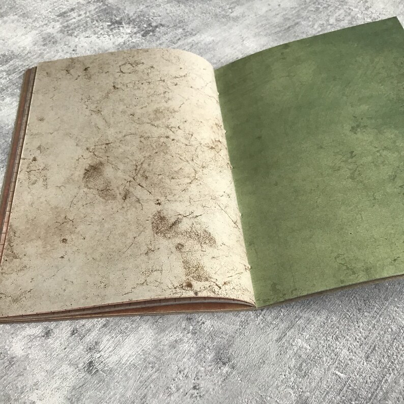 Puede incluir: Un cuaderno abierto con una cubierta texturizada de color blanquecino y una cubierta verde s&oacute;lida. El cuaderno est&aacute; abierto sobre una superficie gris.