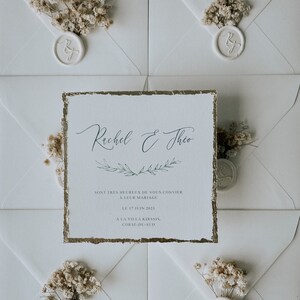 Peut inclure: Une invitation de mariage blanche avec des accents dorés. L'invitation présente les noms "Rachel & Theo" en calligraphie élégante et des détails sur leur mariage le 17 juin 2023, à la Villa Kirssis en Corse-du-Sud.