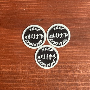 May include: Three black and white round stickers with the text "KEEP EVOLVING" and a graphic of the evolution of humans.