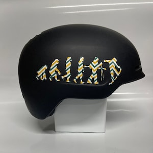 May include: Black ski helmet with a white, yellow, and green evolution of man sticker. The sticker shows a series of stick figures progressing from a primitive ape to a modern human holding a camera.
