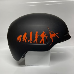 May include: A black ski helmet with an orange evolution of man sticker. The sticker shows a series of figures progressing from a crouching ape to a skier.