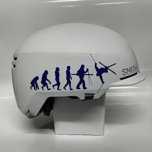 May include: White ski helmet with a blue evolution of man graphic, ending with a skier doing a trick. The helmet has the word "SMITH" on the side.
