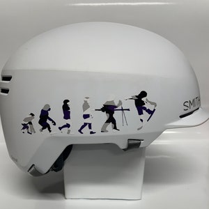 May include: White ski helmet with a black and purple graphic of a line of stick figures skiing down a mountain. The helmet has the word "SMITH" printed on the side.