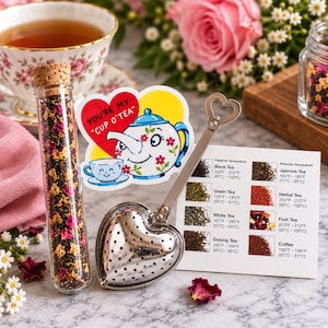 May include: A clear glass test tube filled with loose leaf tea, a heart-shaped metal tea infuser, and a white informational card listing brewing temperatures for various teas. A sticker featuring a cartoon teapot and the text YOU'RE MY CUP O'TEA.
