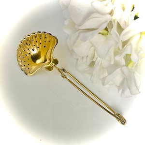 May include: Gold-toned metal tea infuser shaped like a seashell with a long handle. The infuser has a mesh design and is perfect for steeping loose leaf tea.