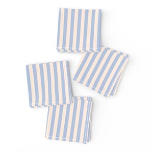 May include: Four folded cloth napkins with a vertical striped pattern. The stripes alternate between light blue and cream. The napkins are arranged on a white background.