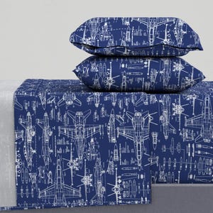 May include: A blue bed sheet and pillowcases with a white print of fighter jet blueprints. The print is repeated all over the bedding.