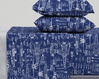May include: A blue bed sheet and pillowcases with a white print of fighter jet blueprints. The print is repeated all over the bedding.