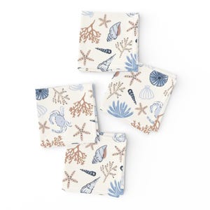 May include: Set of four white cotton napkins with a blue and brown sea life pattern. The pattern includes starfish, seashells, coral, and a crab.