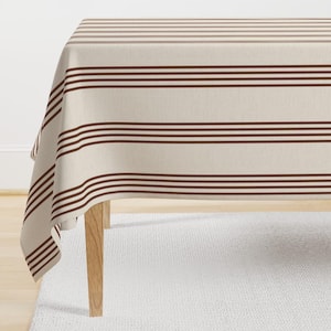 Puede incluir: Un mantel de mesa a rayas marrones y blancas con una textura de lino sutil. El mantel está drapeado sobre una mesa de madera con una alfombra blanca debajo.