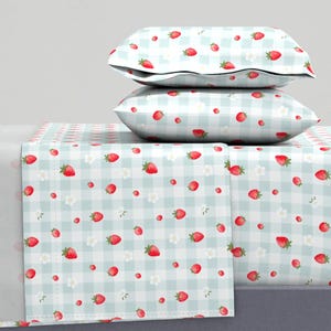 May include: A bedding set featuring a light blue and white gingham pattern. The set includes a flat sheet, fitted sheet, and two pillowcases. The sheets and pillowcases are decorated with red strawberries and small white flowers.