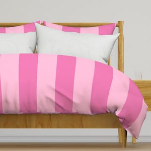 May include: A bed with a wooden frame and a pink and light pink striped duvet cover. Two white pillows are visible, along with a matching striped pillowcase. The bedding is neatly arranged, suggesting a clean and inviting bedroom setting.