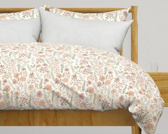 Puede incluir: Una funda nórdica blanca con un estampado floral en tonos rosa, melocotón y gris. La funda nórdica está sobre un marco de cama de madera.