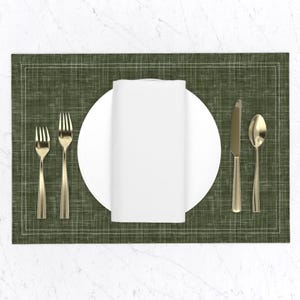 May include: A green placemat with a white border and a white linen napkin, a white plate, a gold fork, a gold knife, and a gold spoon.
