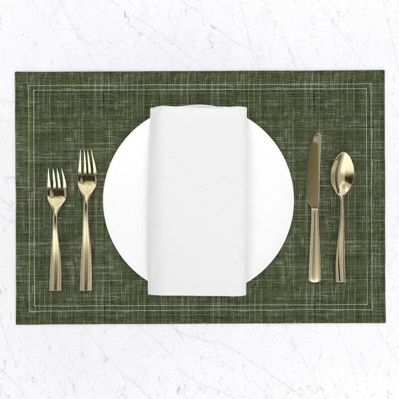 May include: A green placemat with a white border and a white linen napkin, a white plate, a gold fork, a gold knife, and a gold spoon.