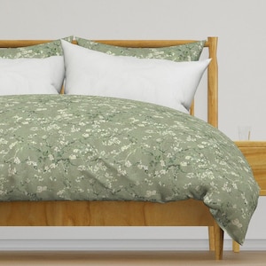 Può includere: Un letto con struttura in legno e un copriletto e federe verde salvia. Il copriletto e le federe presentano un motivo floreale bianco. Il letto è composto da cuscini bianchi.