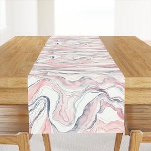 May include: A pink and gray marble patterned table runner. The runner has a white background with pink and gray swirls and lines.