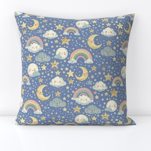 Puede incluir: Una almohada azul con un patrón repetido de estrellas, lunas, nubes y arcoíris. El patrón está en tonos de amarillo, rosa y azul.