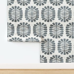 May include: Wallpaper roll featuring a repeating pattern of stylized, gray-blue leaf-like shapes on a cream-colored background. The design has a textured appearance, with a slight distressed effect, adding visual interest to the surface.