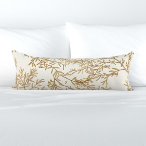 以下が含まれることがあります： 金色に花柄が描かれた長い白い枕。枕は柔らかく快適な生地で作られており、どんな部屋にも上品さを加えるのに最適です。