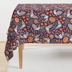 May include: A dark blue tablecloth with a repeating pattern of bats, pumpkins, and flowers in shades of orange, pink, and white. The tablecloth is made of a soft, durable fabric and is perfect for adding a touch of whimsy to your Halloween decor.