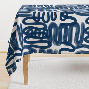 May include: A white tablecloth with a navy blue abstract pattern of squiggly lines. The tablecloth is draped over a wooden table.