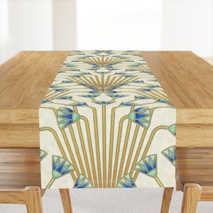 May include: A white table runner with a geometric pattern of blue, green, and gold stylized lotus flowers. The pattern is repeated across the runner.