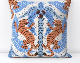 May include: Decorative square pillow with a repeating pattern of orange tigers, blue palm leaves, and a central palm tree design. The background is a cream color with small blue dots. The tigers are roaring and have black stripes.