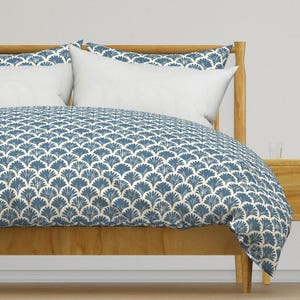 May include: A white duvet cover with a blue fan-shaped pattern. The duvet cover is on a wooden bed frame with two white pillows.