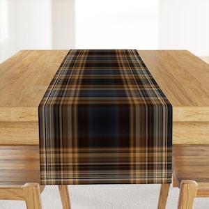 May include: A brown and black plaid table runner with a subtle sheen. The runner is placed on a wooden table.